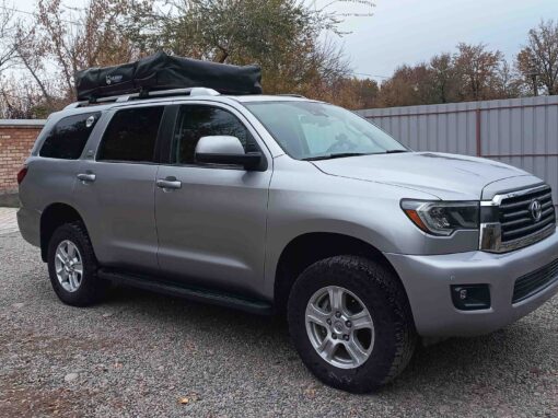 Un SUV Toyota Sequoia argenté, équipé d'une tente de toit noire, garé sur une allée en gravier lors d'un voyage en 4x4 au Kirghizistan.