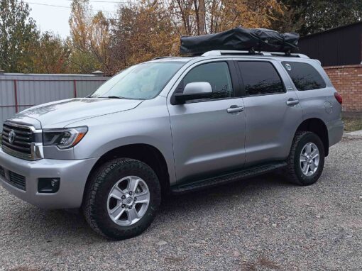 Un SUV Toyota Sequoia argenté, équipé d'une galerie de toit et d'un porte-bagages, garé sur un parking en gravier lors d'une excursion en 4x4 au Kirghizistan.