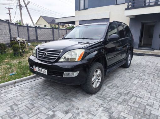 vlad-4x4-rental-bishkek-lexus (1) A black Lexus SUV is parked on a paved driveway in front of a modern house with gray walls and a stone fence. The vehicle's front license plate displays 968 AUT.