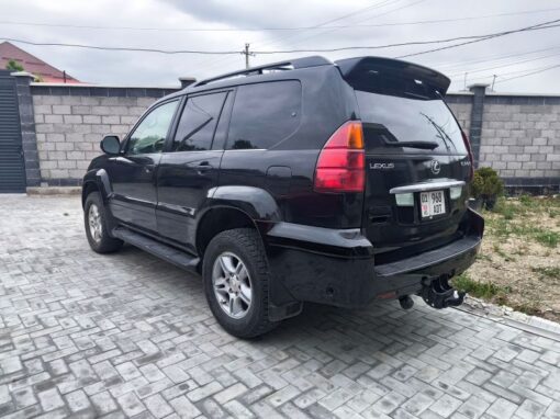 vlad-4x4-rental-bishkek-lexus (13) A black Lexus SUV is parked on a paved driveway next to a gray brick wall, with a cloudy sky overhead and a house partially visible in the background.