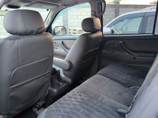 vlad-4x4-rental-bishkek-lexus (2) The image shows the interior of a car, focusing on the rear seat with gray upholstery. The front seats are visible and the car door is opened, revealing part of a brick wall and another vehicle outside.